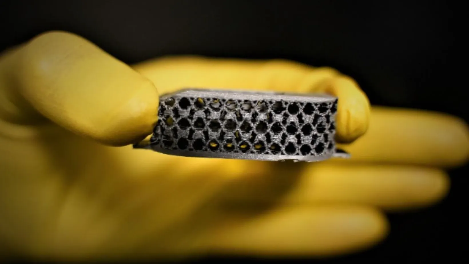 A gloved hand holding a 3D-printed lattice interbody fusion cage